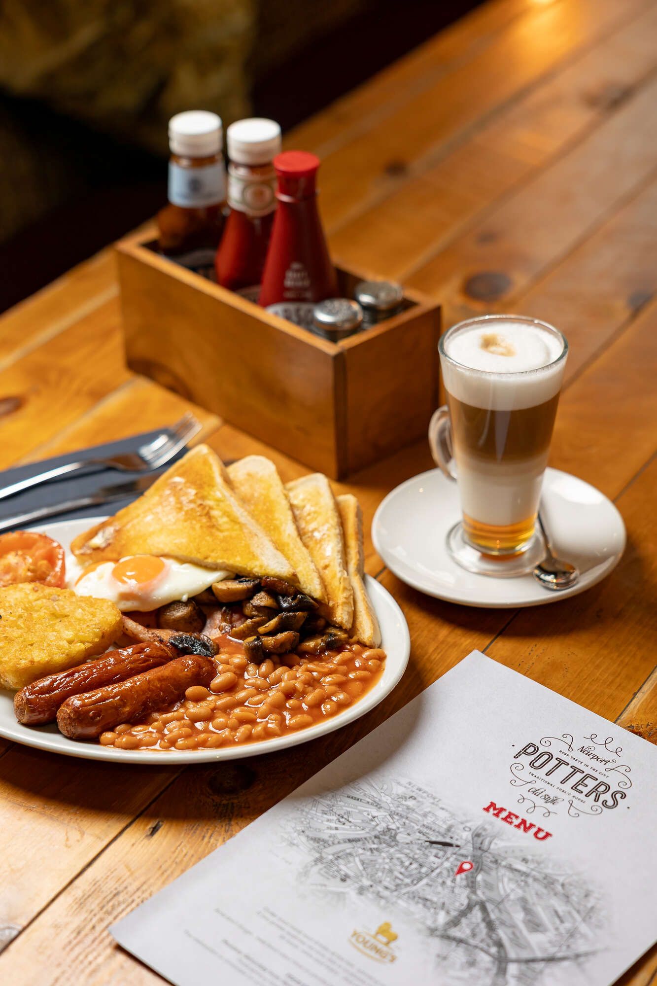 table with Latte, sauaces & full english - bacon, egg, Sausage, baked beans, hash browns & toast